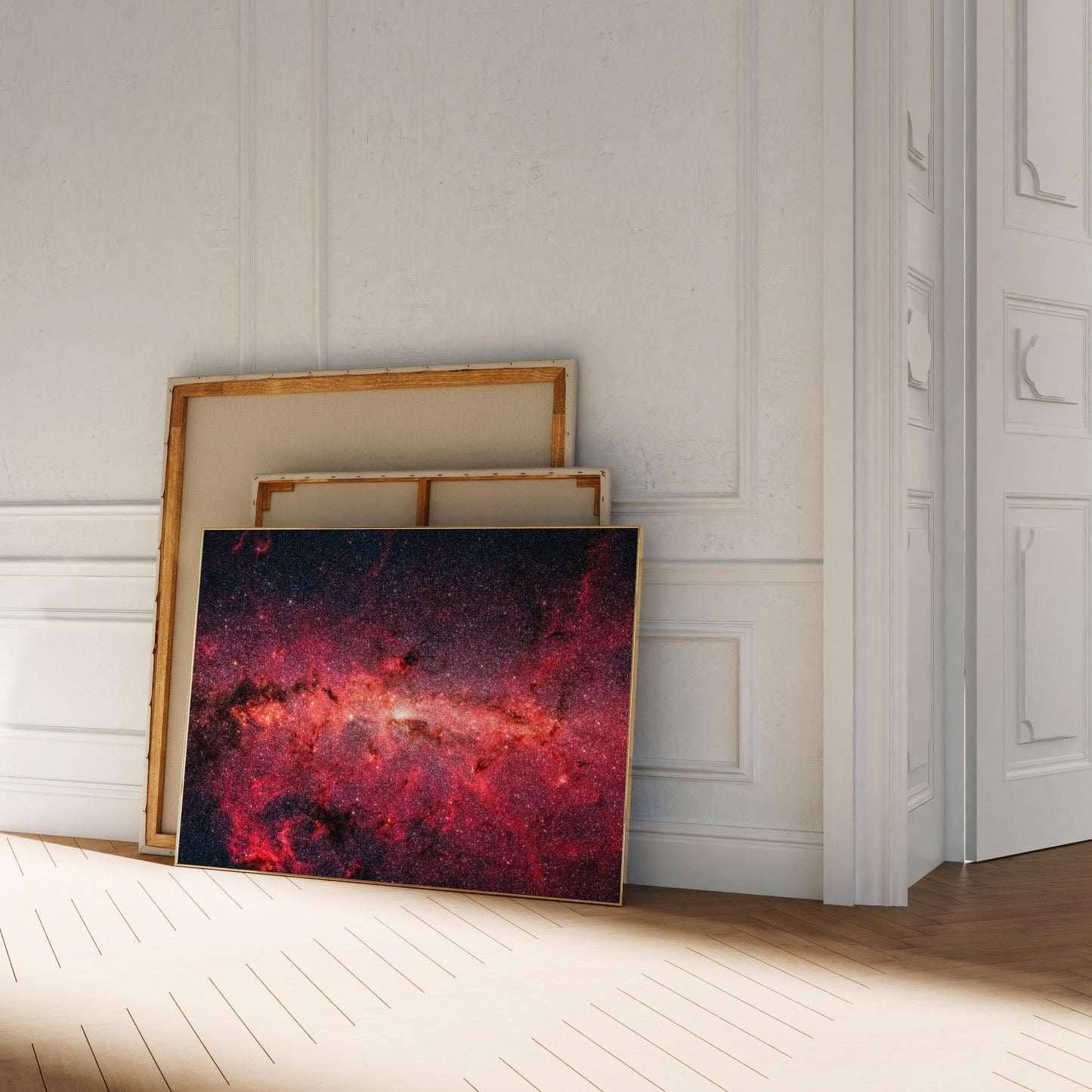 a large, vibrant painting of a galaxy, with a dark background and a bright, colorful foreground. The painting is leaning against a white wall, and there are other paintings stacked on top of it.