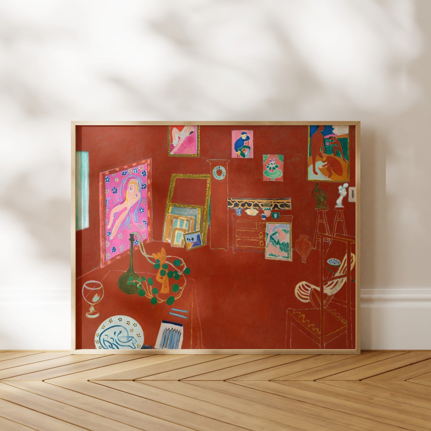 The image is a framed painting depicting a room with various objects, including a vase, a chair, and a table. The painting has a vibrant color palette and is displayed on a wooden floor against a white wall.