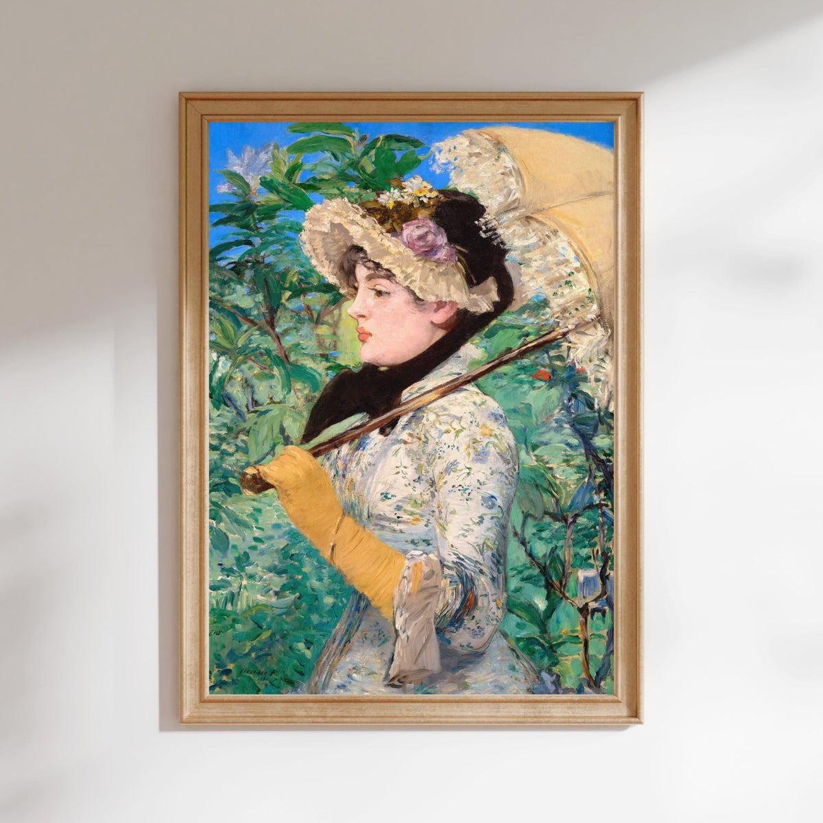 A framed painting depicting a woman wearing a hat and holding an umbrella, standing in a garden setting with lush greenery in the background.